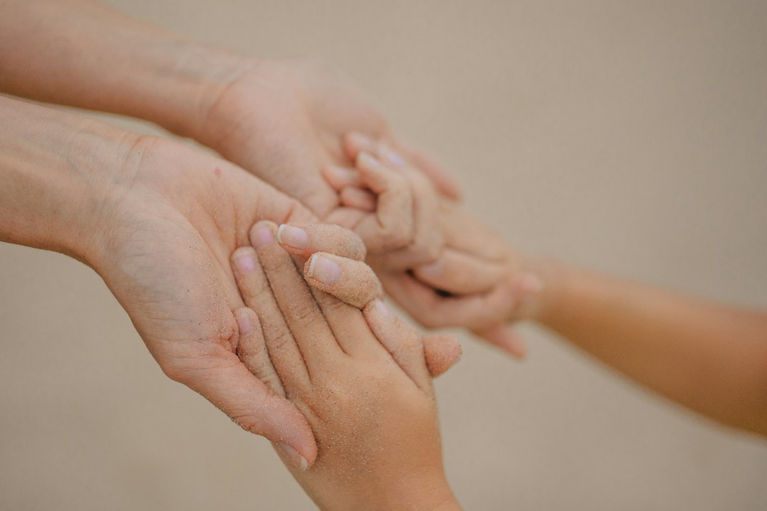 A child's small hands gently hold an adult's open hands.